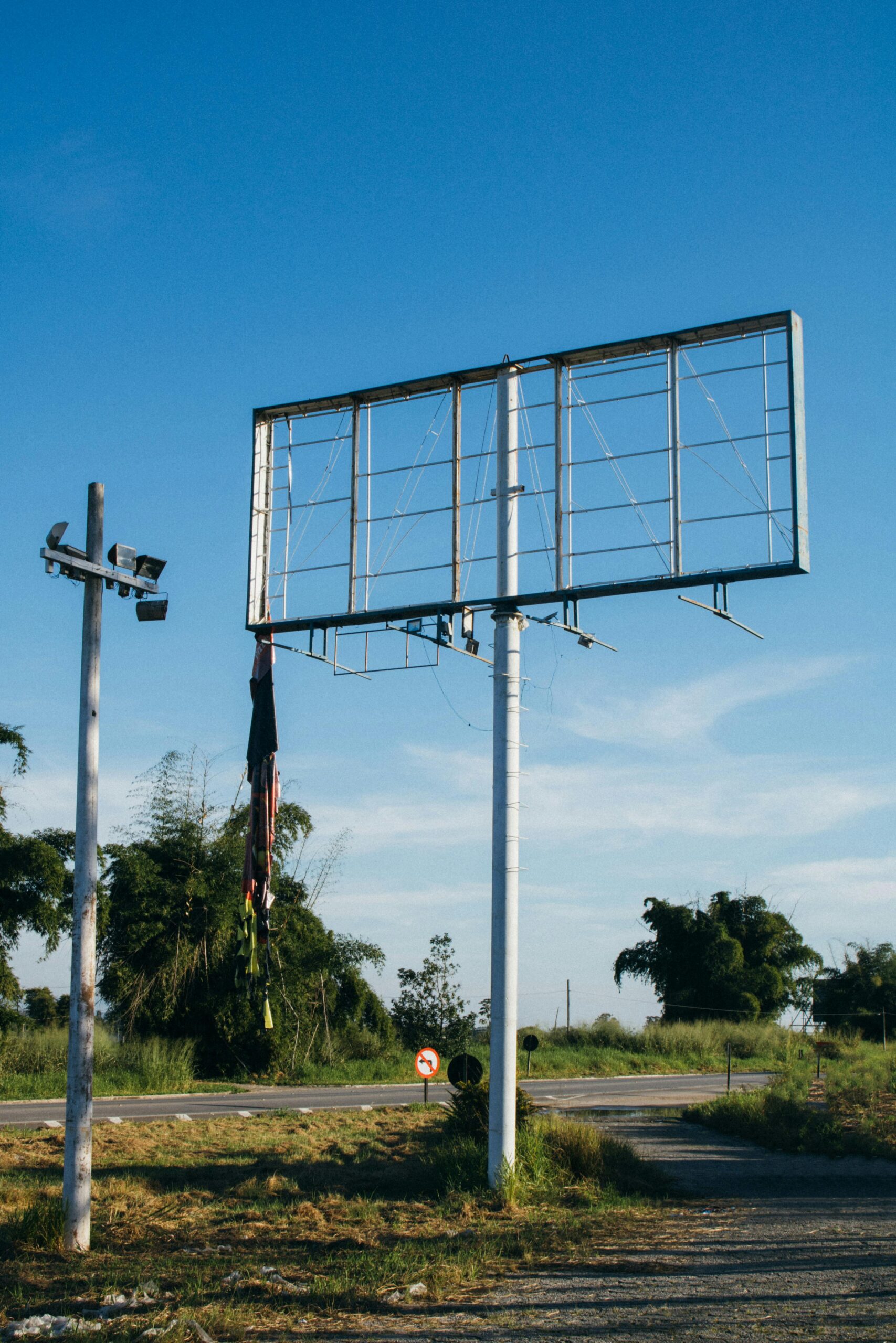 An empty metal billboard structure stands tall on a rural road under a clear blue sky.